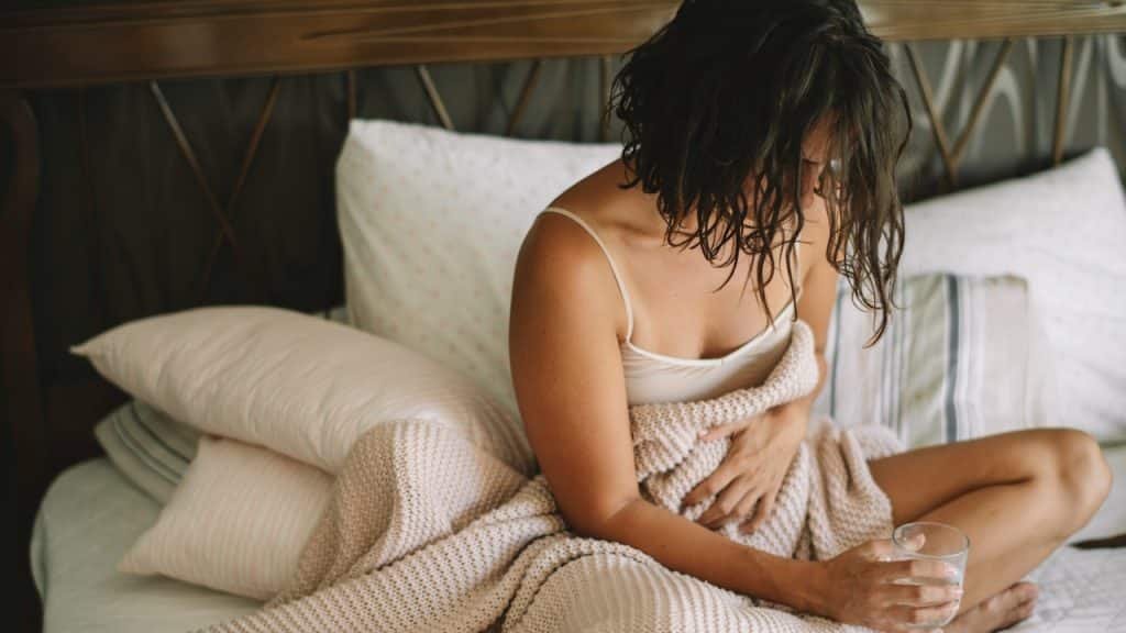 A young woman sitting on a bed having stomach pain.