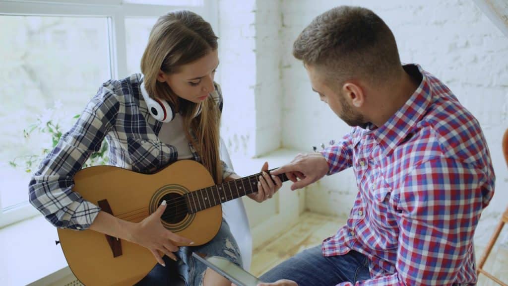 A man teaching a woman to play guitar indoors.