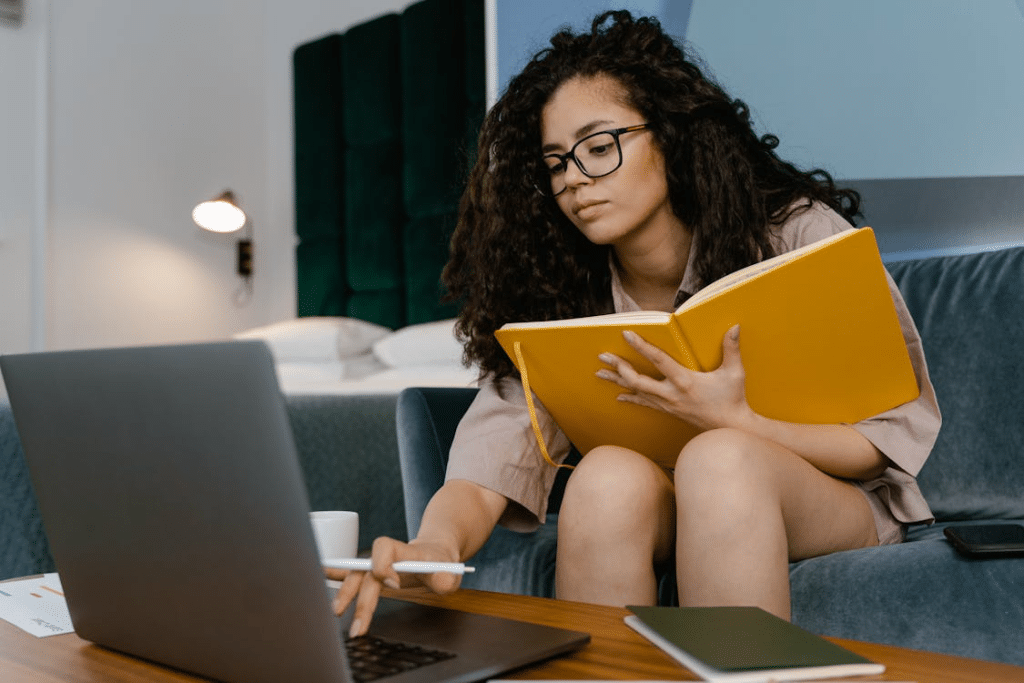 A woman holding a book and using a laptop