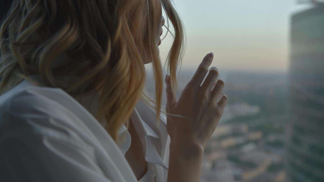 A person standing by a window, gently touching the glass while looking outside.