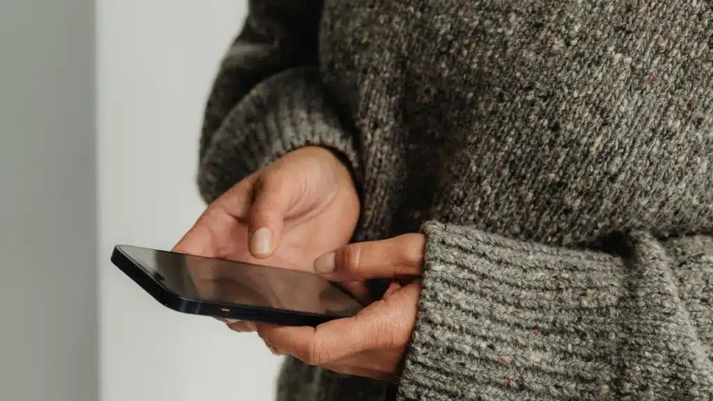 A person wearing a gray sweater holding a smartphone.