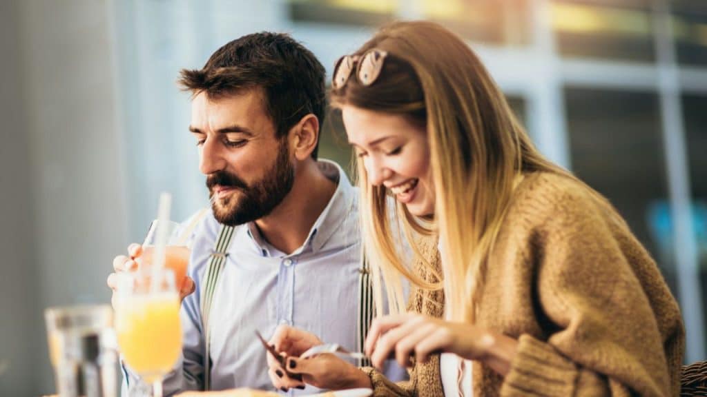 A man and a woman smiling and looking down while sitting at a table.