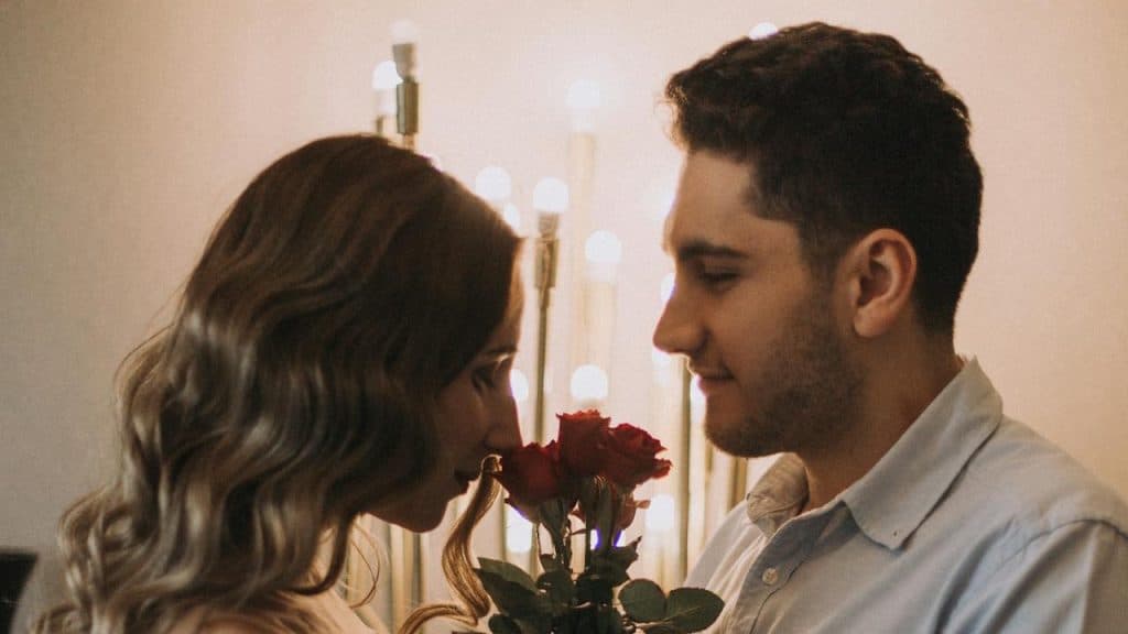 A couple standing close together with roses between them.