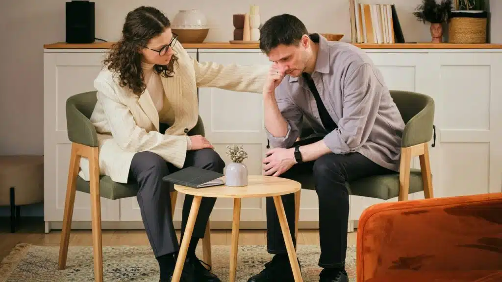 A woman comforting a distressed man seated across a small table.