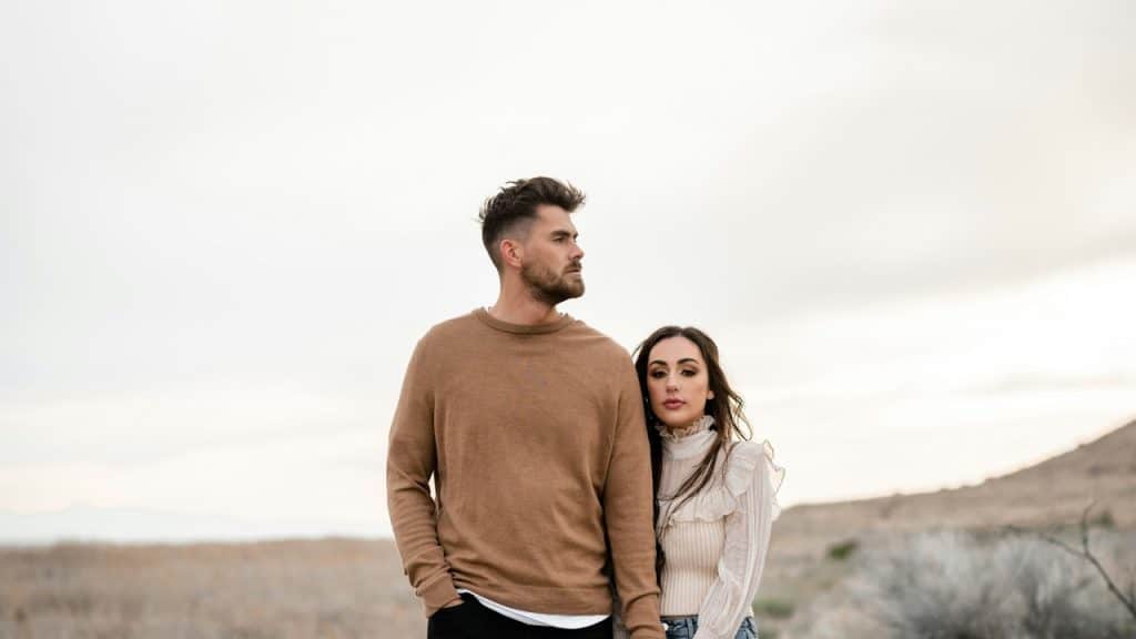 A couple standing outdoors and holding hands while standing close together.