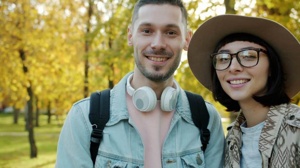 A smiling couple poses outdoors in autumn.