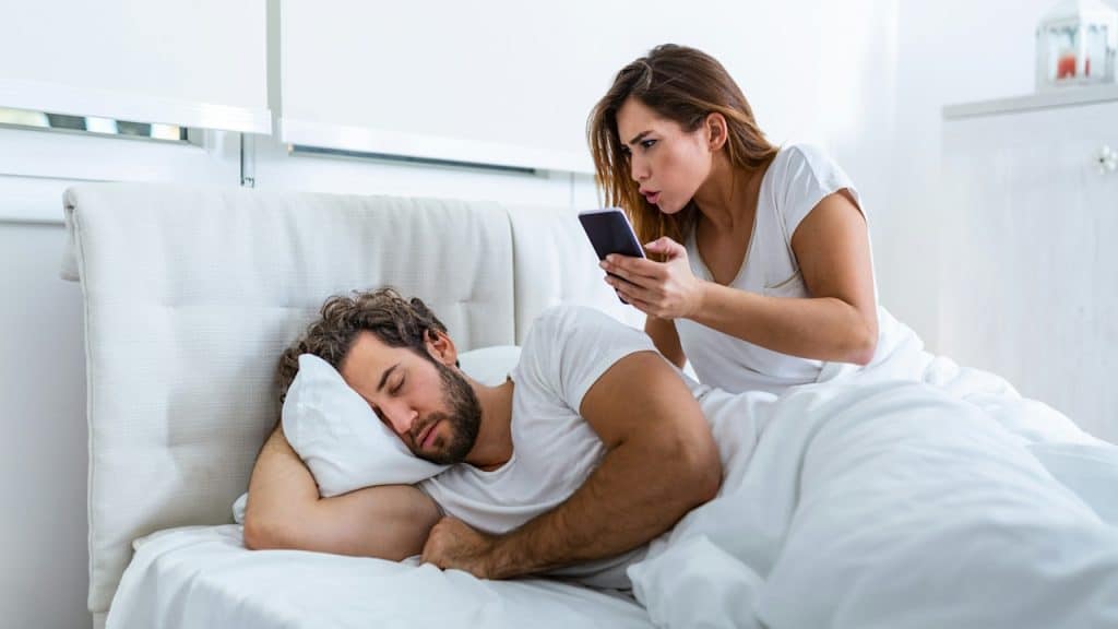 A woman spying on her husband’s phone while he is sleeping.