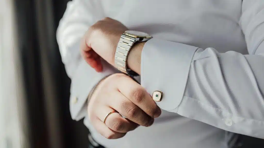 A man adjusting his shirt cuff while wearing a watch.
