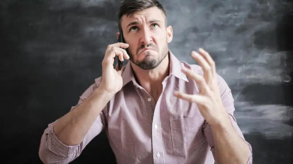 A man talking on the phone with a frustrated expression and raised hand.