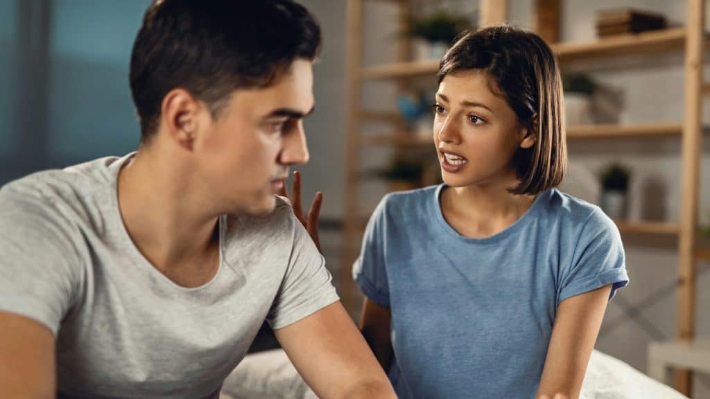 A young woman is arguing and gesturing with her hand at a man sitting next to her, who looks away.