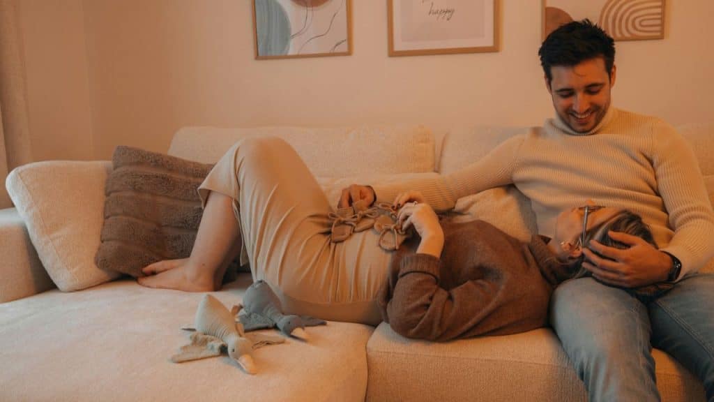 A smiling man on a couch gently strokes the hair of a woman reclining beside him.