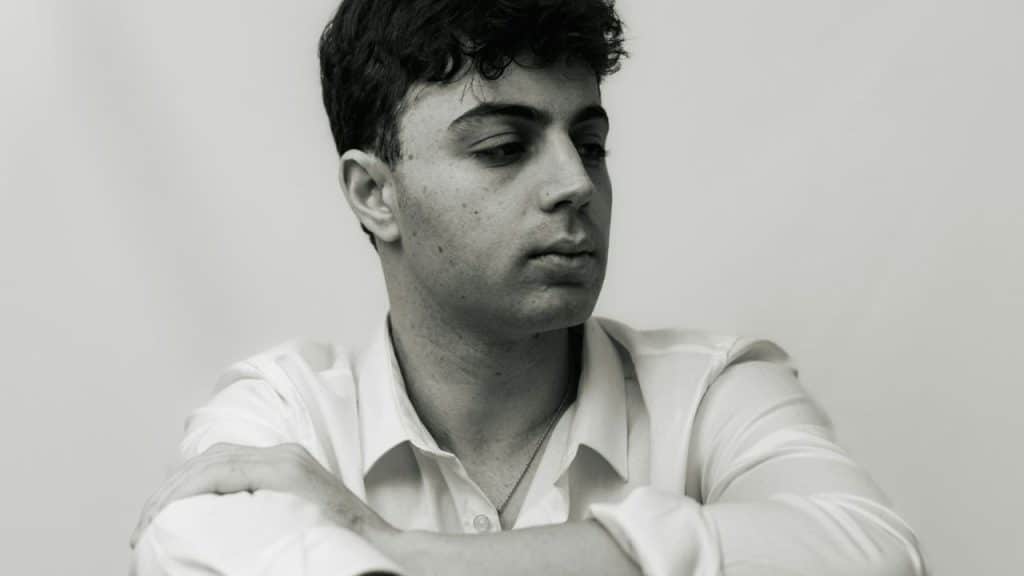Black and white portrait of a young man in a white shirt, arms crossed.