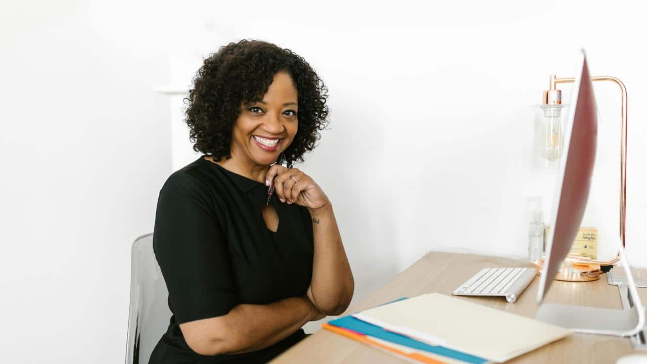 A woman in a black dress smiling while sitting at her desk.