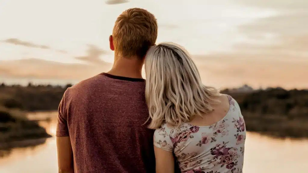 A couple standing together and watching the sunset by the water.
