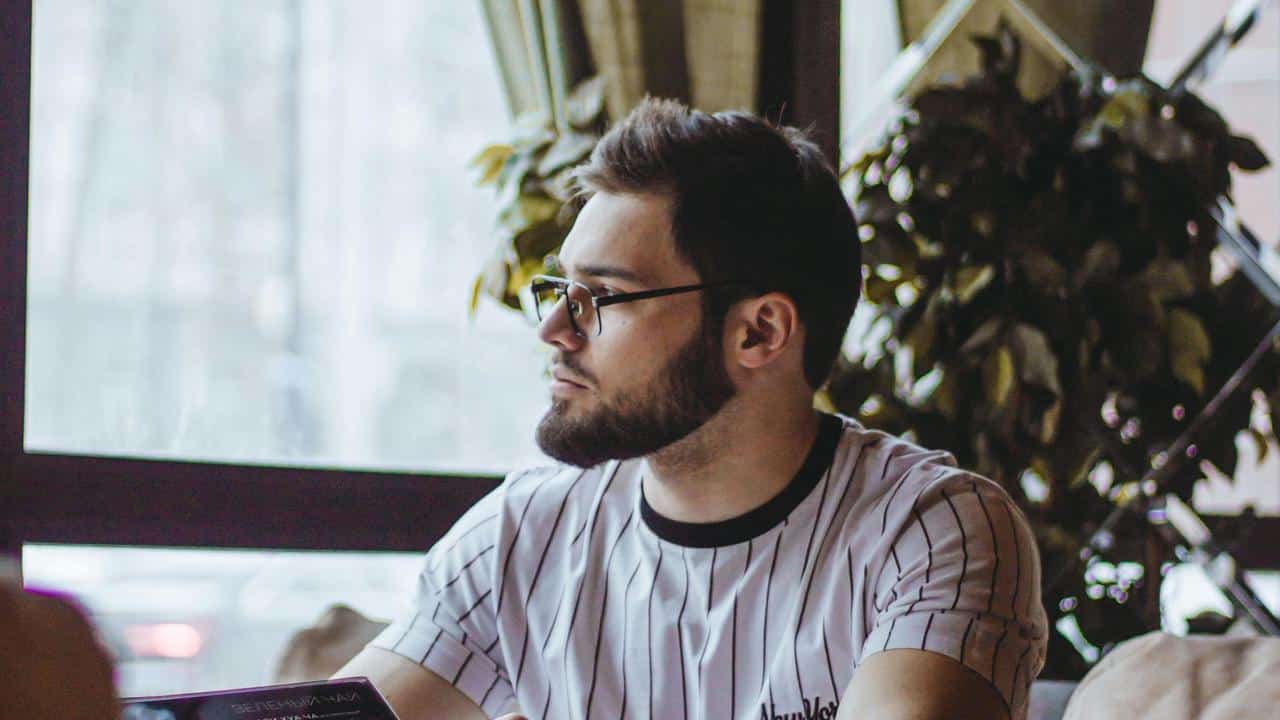A man wearing glasses sitting indoors and looking to the side.