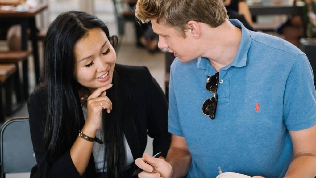 A man and woman sitting together talking and looking at a notebook.