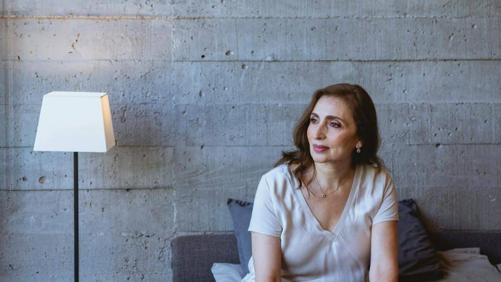 A woman sitting on a sofa beside a floor lamp, looking thoughtfully to the side.