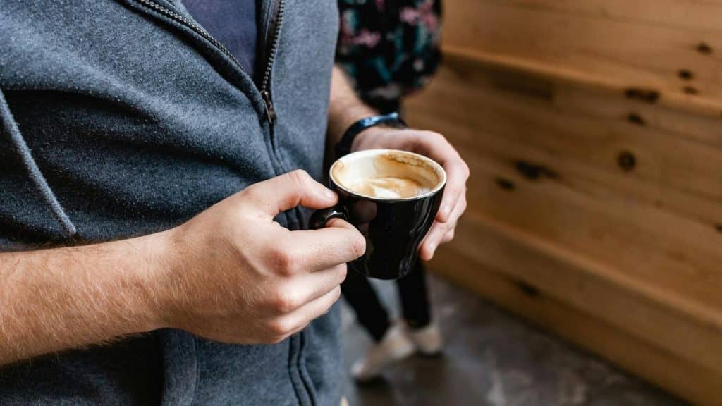 A person holding a black coffee cup filled with cappuccino.