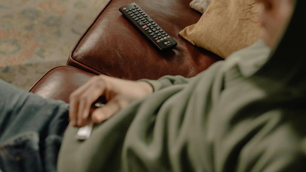 A person reclining on a leather couch with a TV remote nearby.
