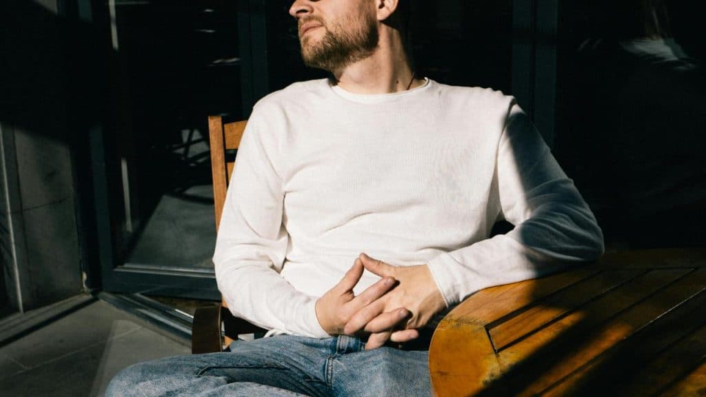 A man in a white shirt sits at a wooden table in sunlight.