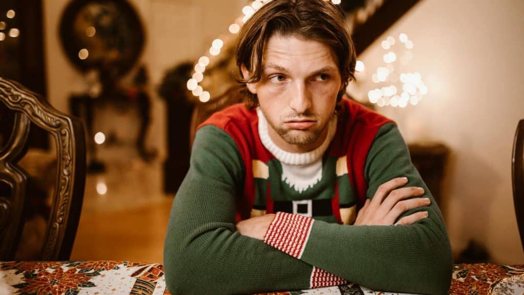 A man wearing red and green sweater, looking bored.