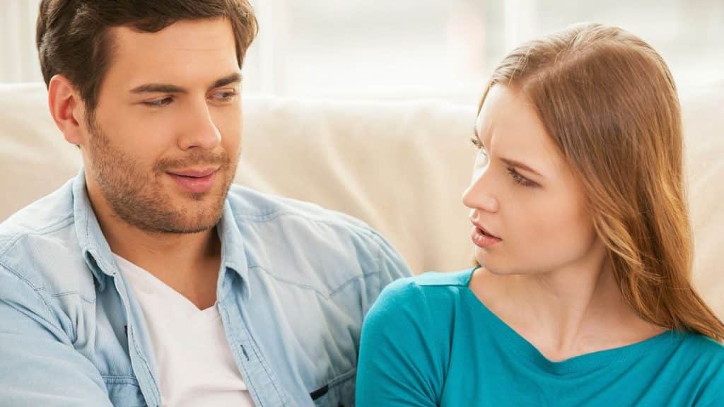 Man smiling slyly next to a woman looking at him with a disapproving expression.