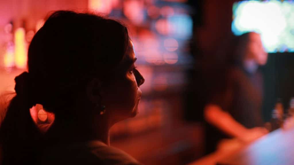 A woman's silhouette in profile at a dimly lit bar, with red and blue background lights.