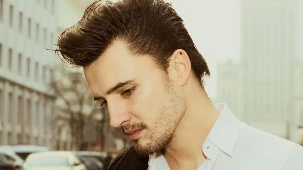 A handsome man in a white formal shirt is looking downwards.