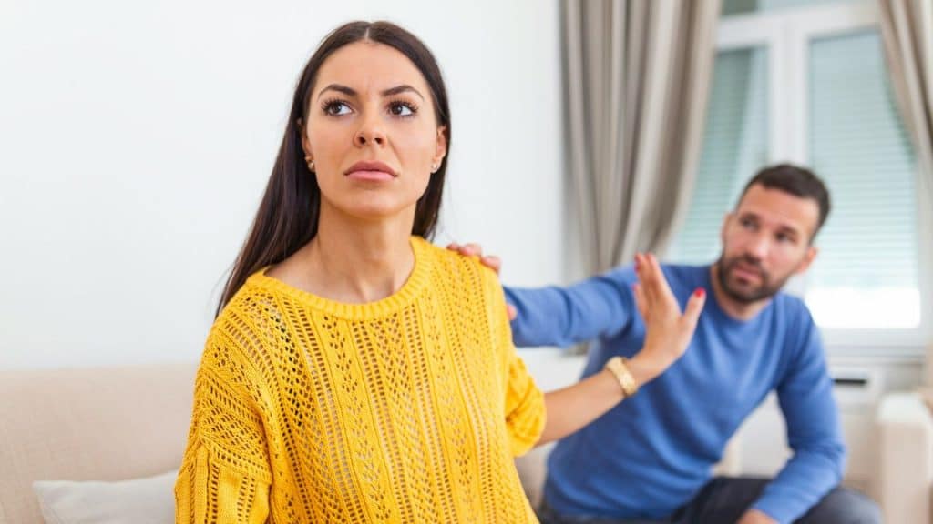 Woman in yellow sweater looks away, man in blue shirt reaches out with an open hand.
