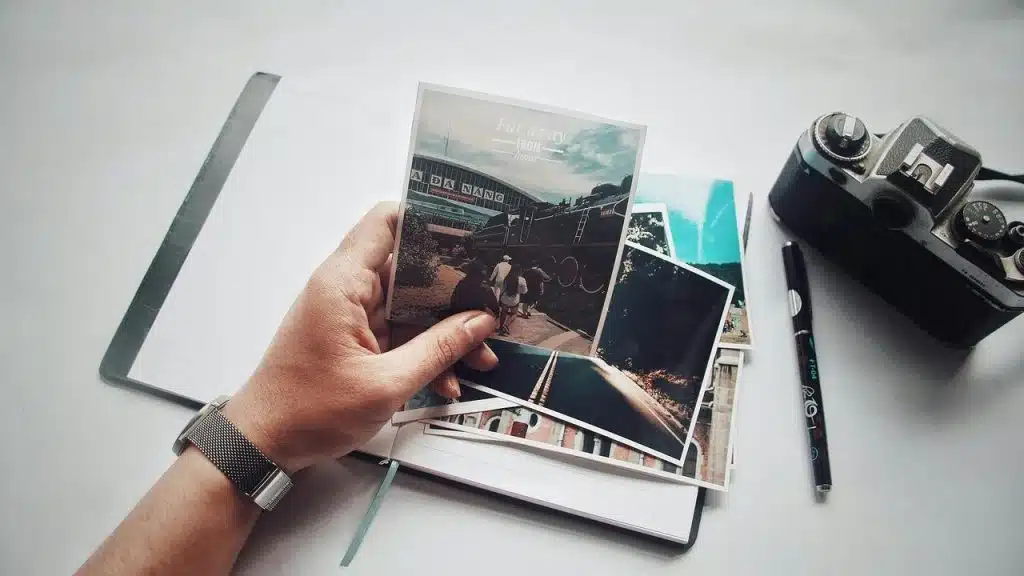 A person holding travel photos over an open notebook with a camera nearby.