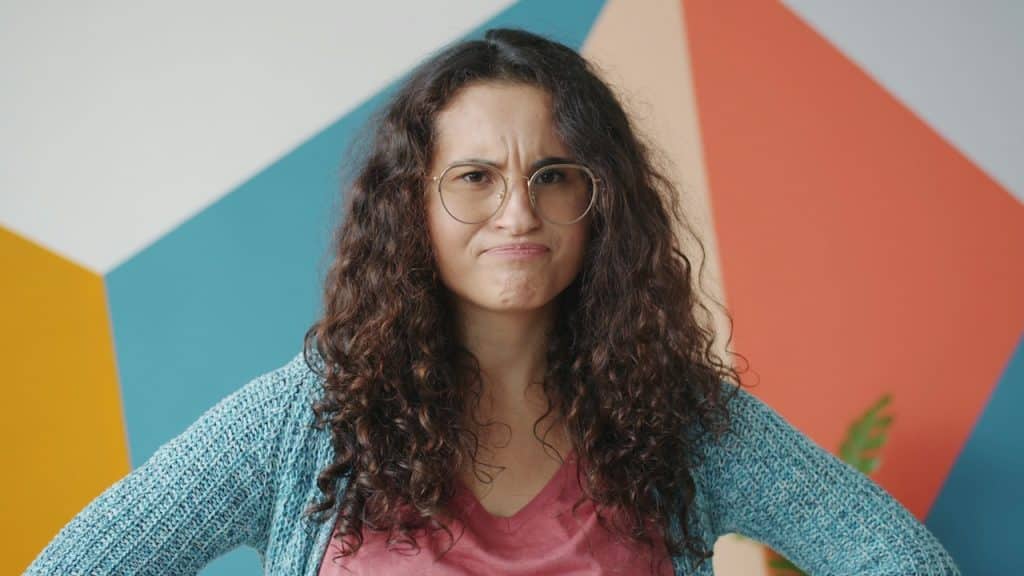 A woman with curly hair and glasses looks annoyed.