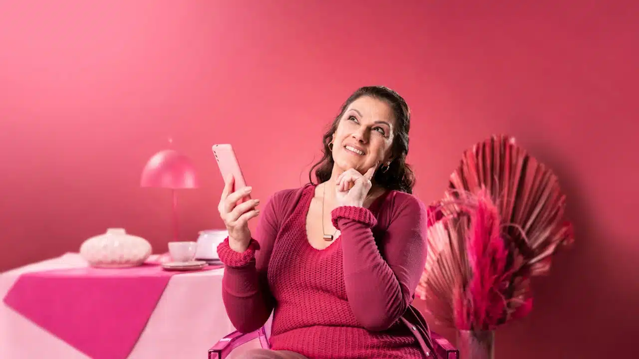 A woman sitting in a red chair holding a cell phone against a red wall.