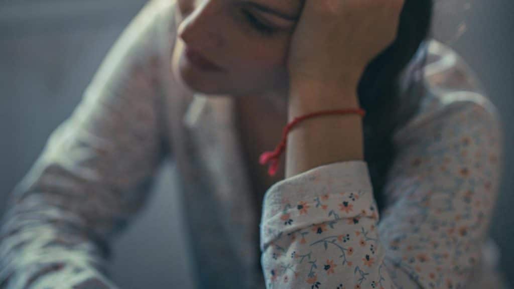 A person resting their head on their hand, wearing a floral shirt.