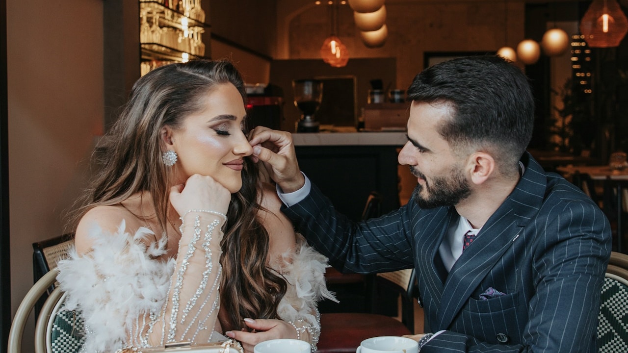 A man touching a woman’s nose pin while sitting at a restaurant.