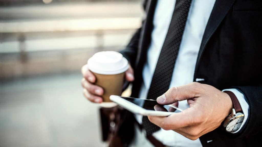 A person wearing a suit holding a coffee cup and a smartphone outdoors.