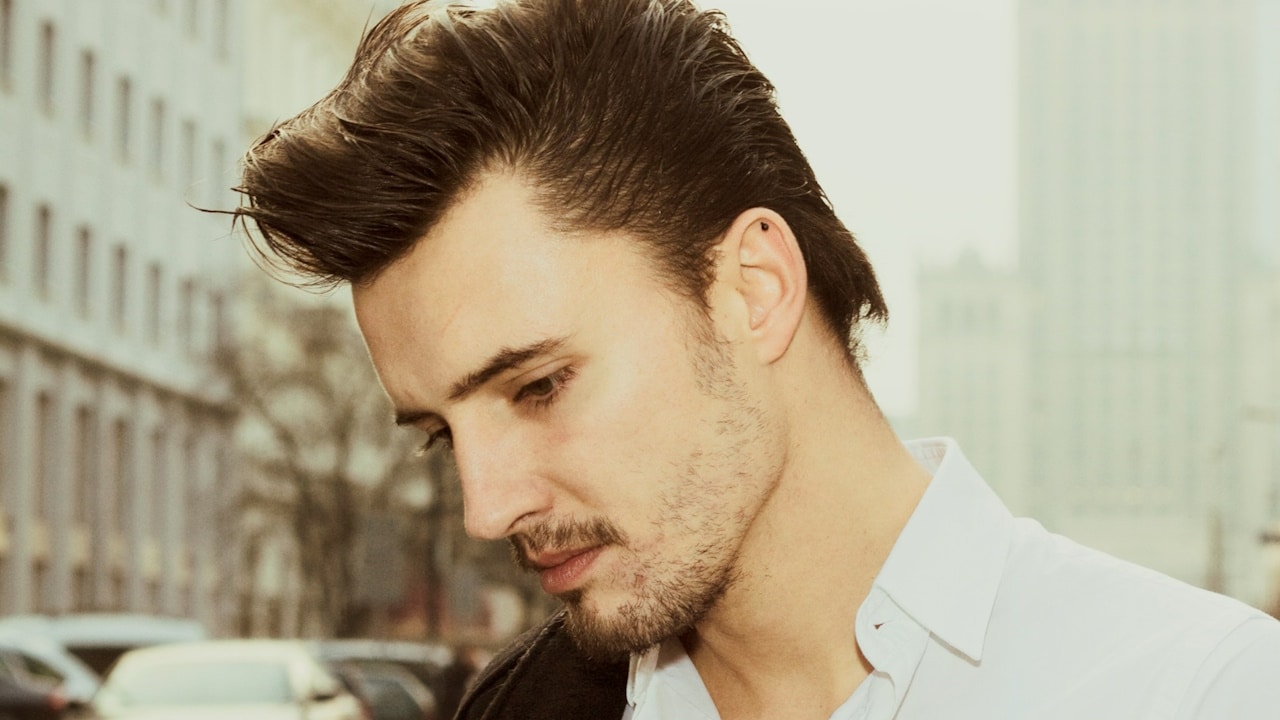 A man looking downwards while standing in the street. 