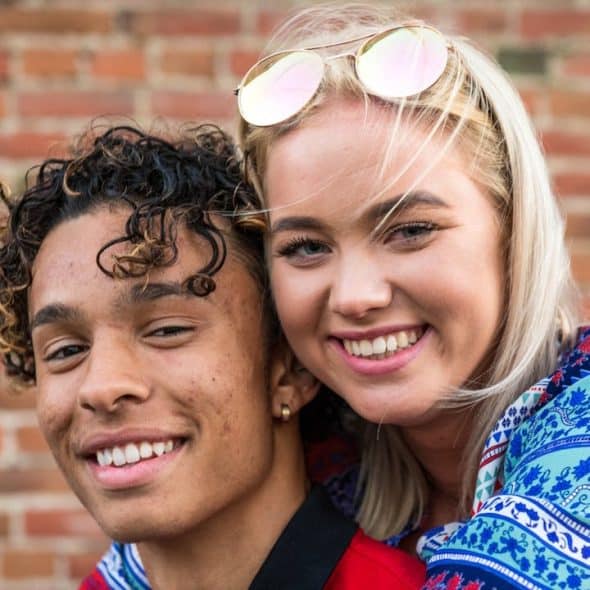 A happy young couple smiling with a brick wall background.