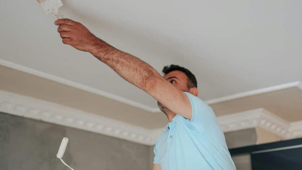 A man painting a ceiling with a brush in a room.