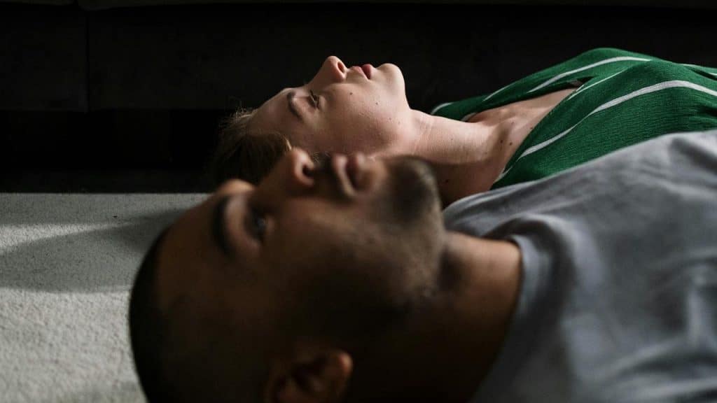 Two people lying on the floor in a dim room with a couch in the background.