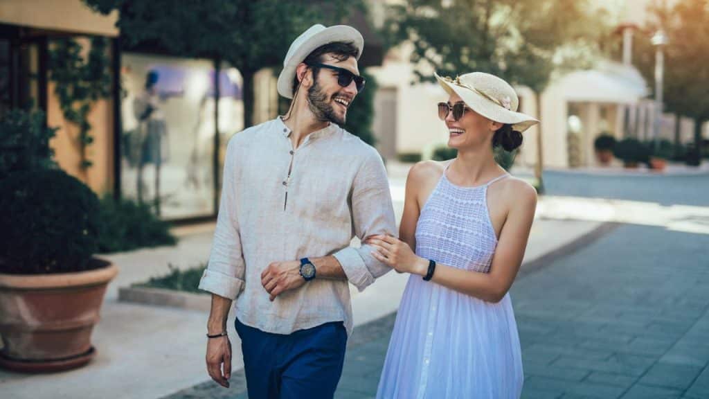 A casually dressed, smiling couple walks arm-in-arm outside on a sunny day.