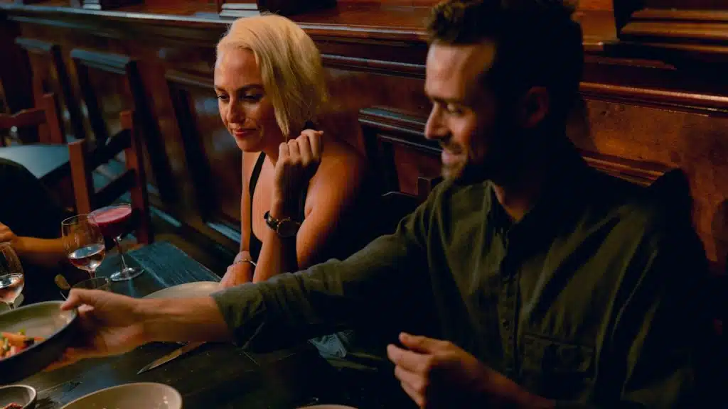 A woman grimacing as a man picks up a plate from in front of her while they are seated at a table.