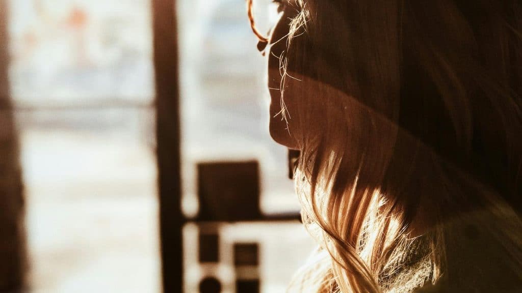 A backlit profile of a woman wearing glasses near a window.