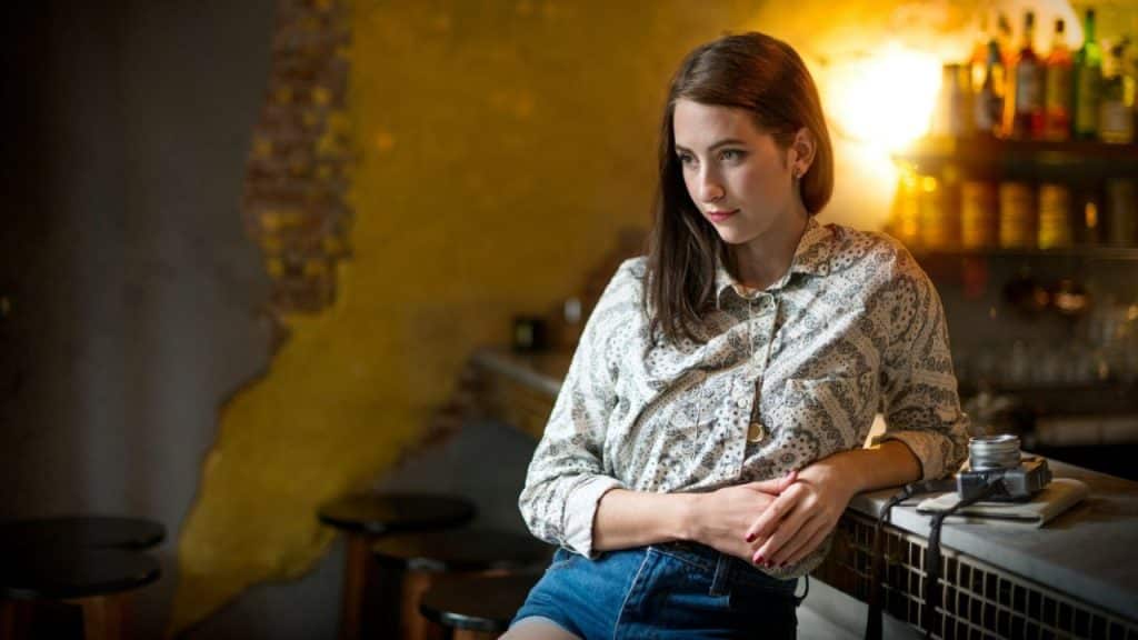 A woman in a paisley shirt leaning on a bar with a vintage camera nearby.