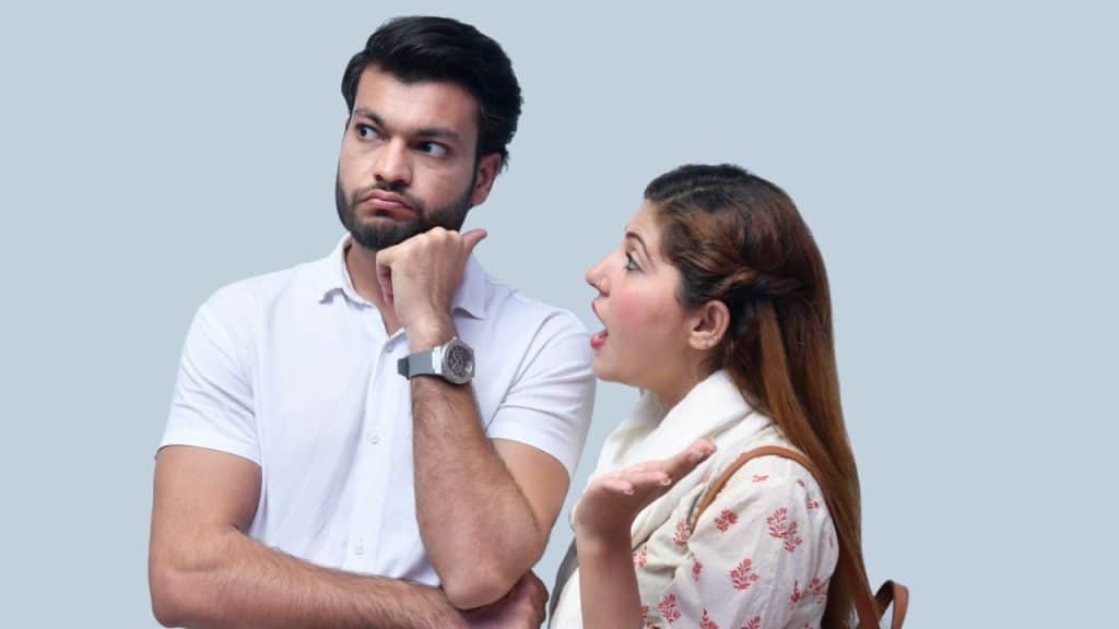 A man looks away with irritation while a woman talks animatedly next to him.