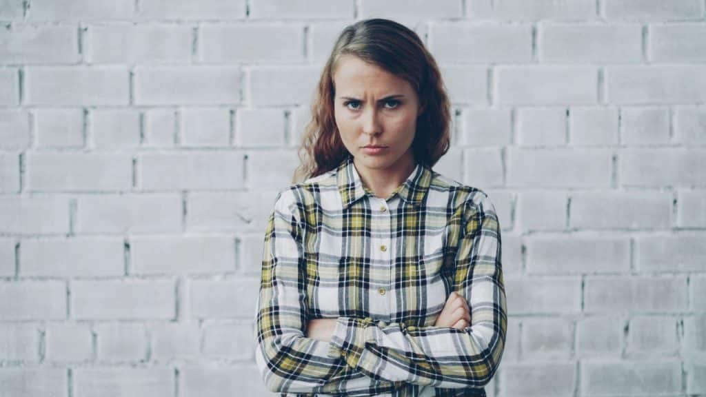 A woman with a serious, displeased expression stands with her arms crossed.