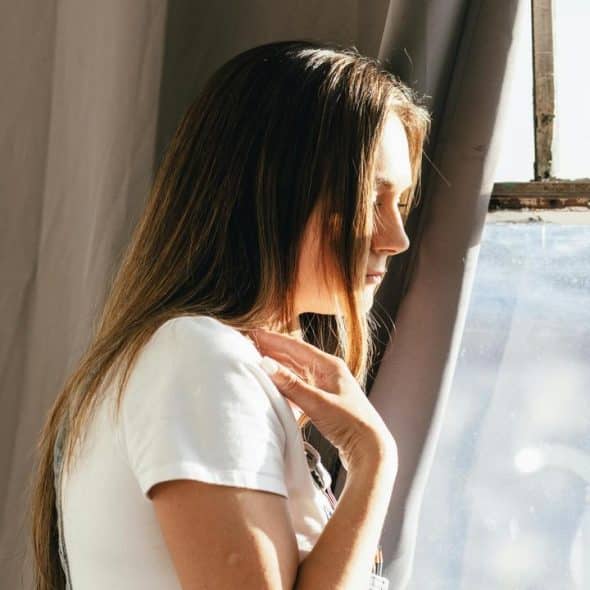 A woman standing by a window in sunlight.