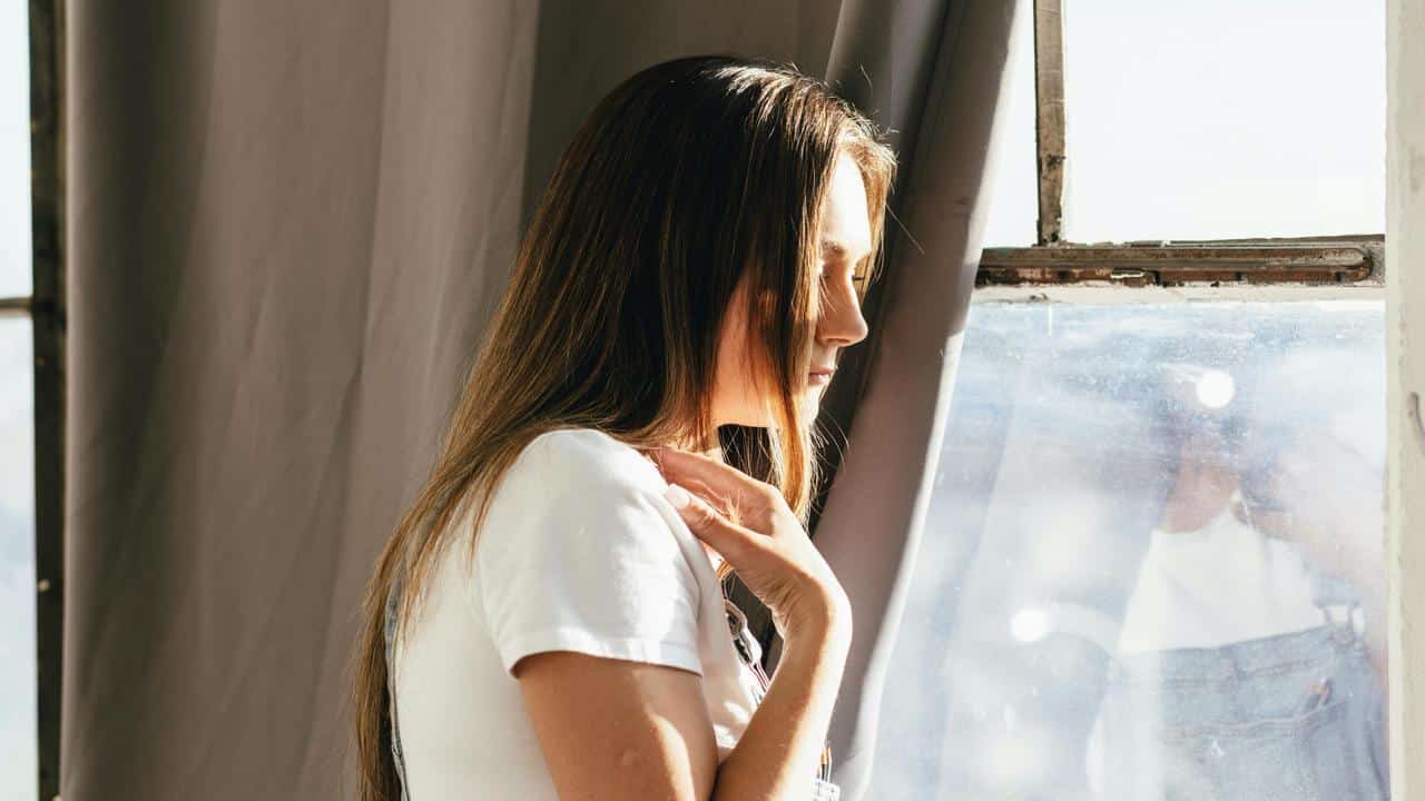 A woman standing by a window in sunlight.