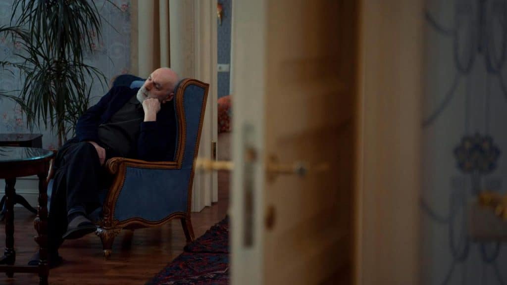 An elderly man resting in an armchair inside a quiet room.