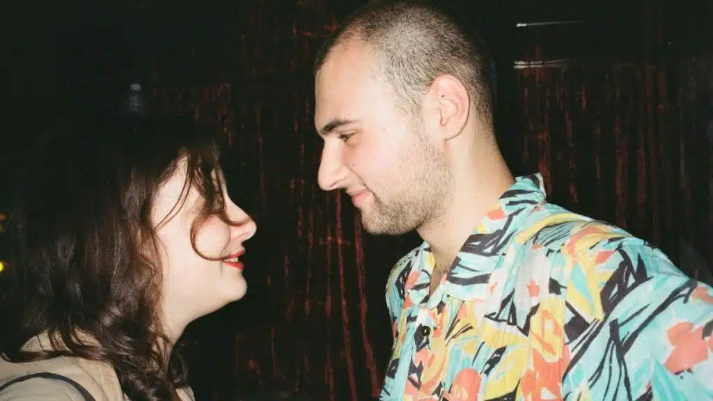 A man in a colorful Hawaiian shirt and a woman with dark, wavy hair looking at each other.