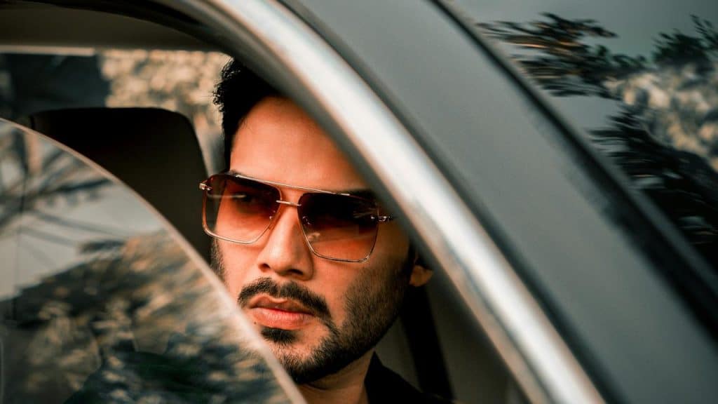 A man wearing sunglasses looking out a car window.